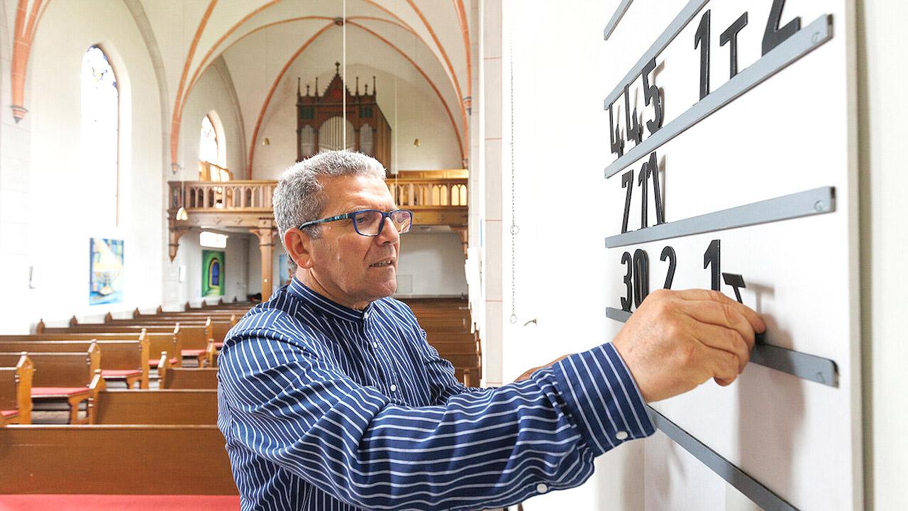 Küster Ein Küster steckt neue Zahlen für die Nummern des Kirchenlieder im Gesangbuch an eine Tafel an der Wand einer Kirche