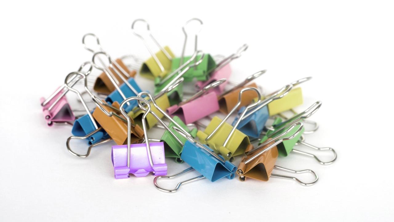 Ein Haufen bunter Foldback-Klammern (Binderclips) in verschiedenen Farben auf hellem Hintergrund.