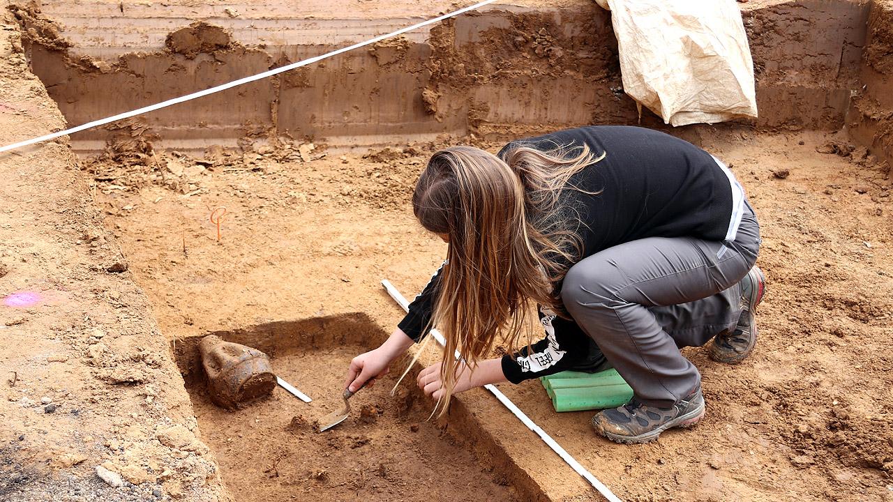 Frau auf einer Ausgrabungsstätte, die mit einer Kelle am Boden kratzt
