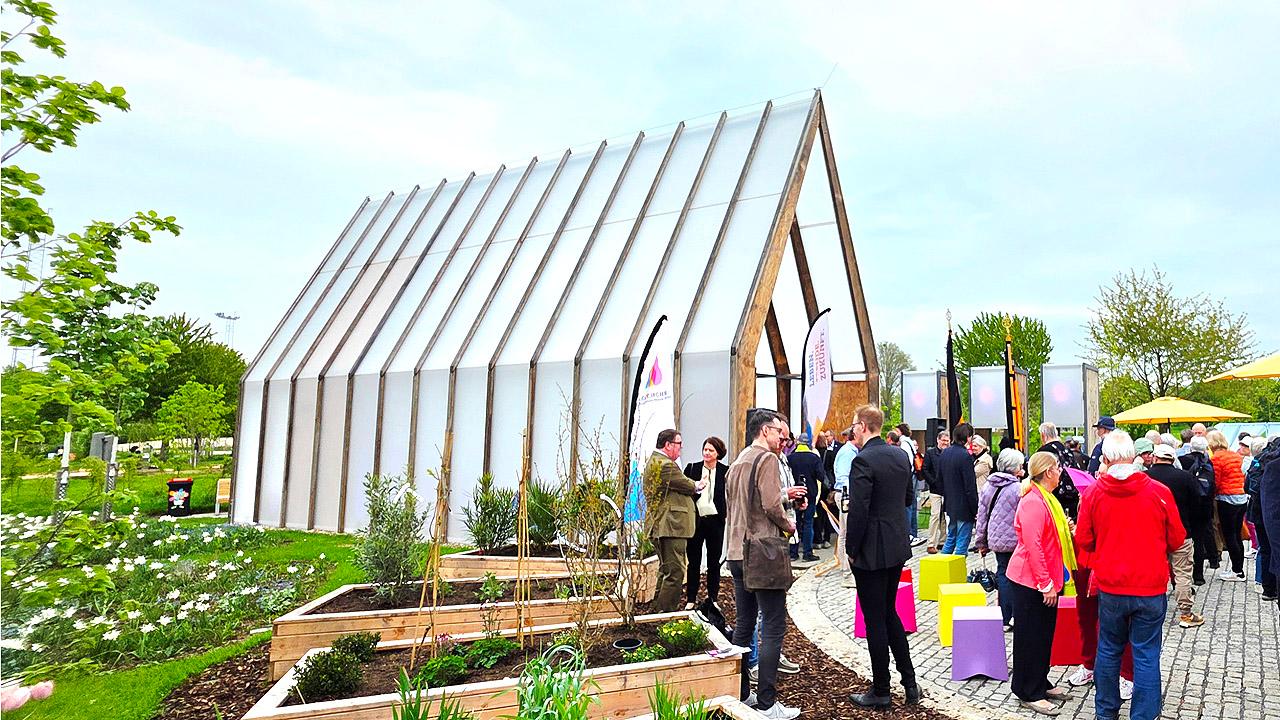 Kleine Kirche mit milchigem Plexiglas, davor Hochbeete und Publikum