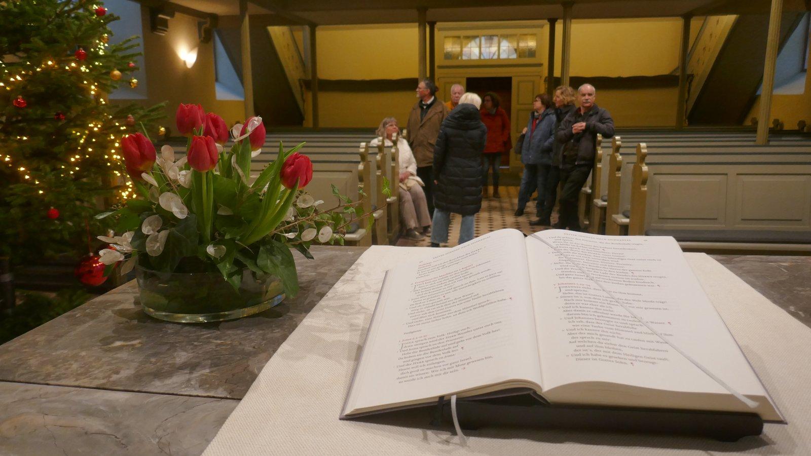 Altar mit Bibel, im Hintergrund der Kirchenraum mit Weihnachtsbaum und Besuchern.
