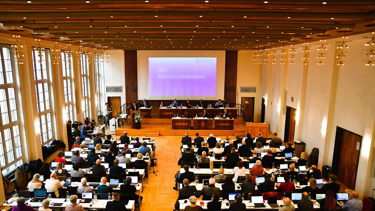 Großer Saal mit Leinwand am Ende, davor viele Bankreihen mit Menschen