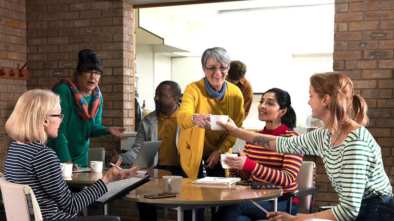 Jüngere und Ältere Menschen sitzen um einen Tisch herum und trinken Kaffee