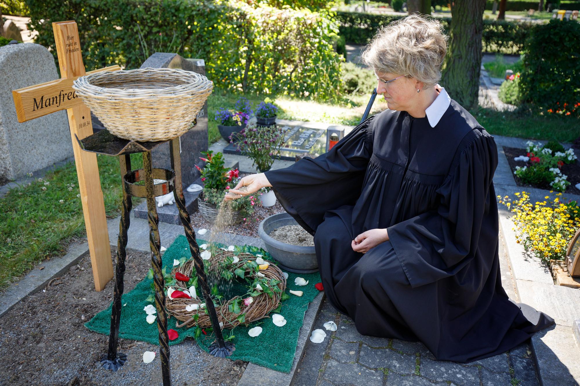 Pfarrerin streut Erde in ein Urnengrab
