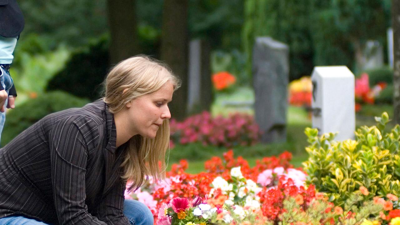 Eine junge Frau an einem Grab mit Blumen