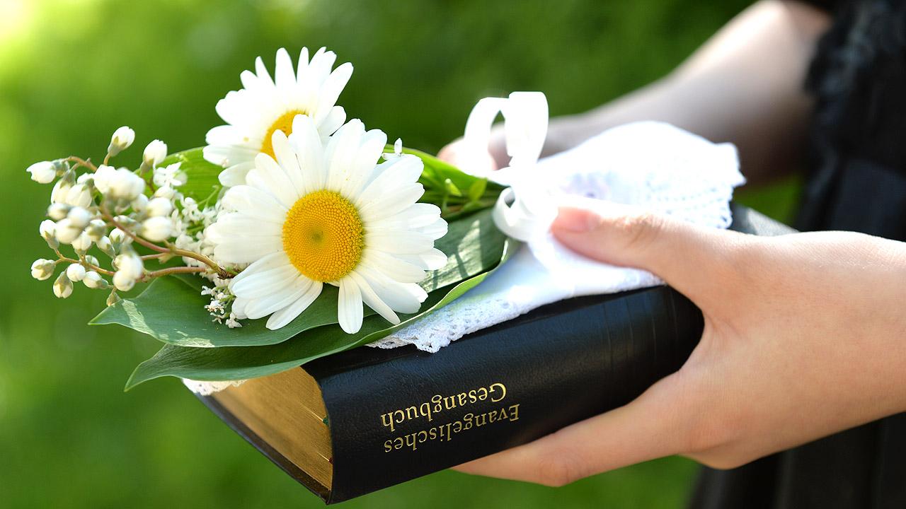 Hand, die einen Blumenstrauß und ein Gesangbuch hält