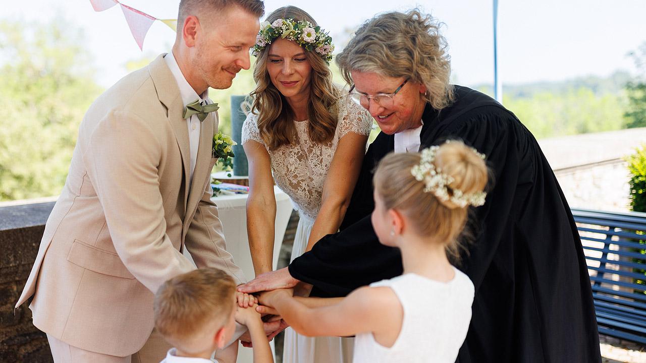 einfach heiraten Hochzeitspaar, 2 Kinder und eine Pfarrerin legen die Hände übereinander