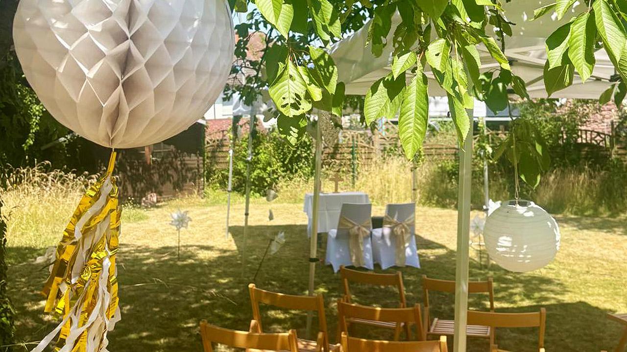 Hochzeit Garten Zwei Stühle mit weißen Hussen und Schleife in einem Garten, davor die Besucherstühle