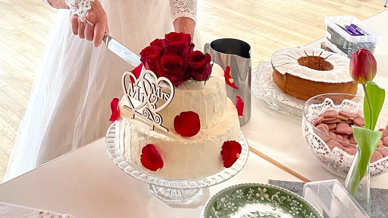 Eine Braut schneidet eine zweistöckige, weiße Hochzeitstorte mit roten Rosen an