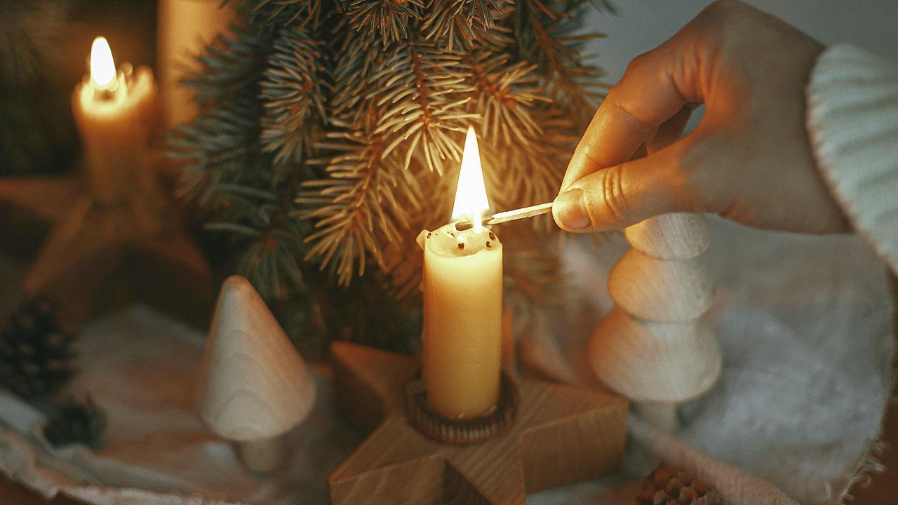 Besinnung im Advent Eine Frau zündet eine Kerze an, daneben Holzdeko in Form von Tannenbäumen und ein Tannenzweig