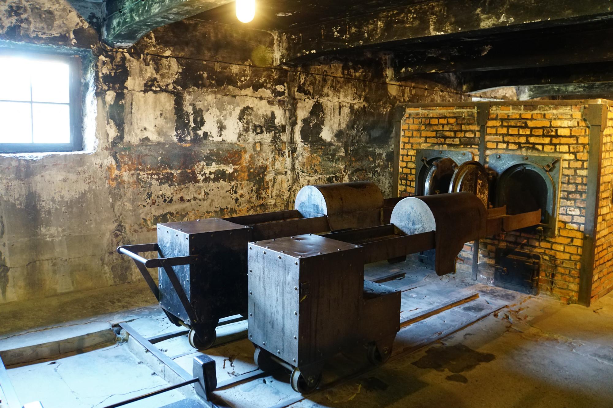 Krematorium Auschwitz Zu sehen ist ein schäbiger Innenraum, in welchem sich Geräte zur Kremation befinden, z. B. ein Ofen mit dazugehöriger Schiene.