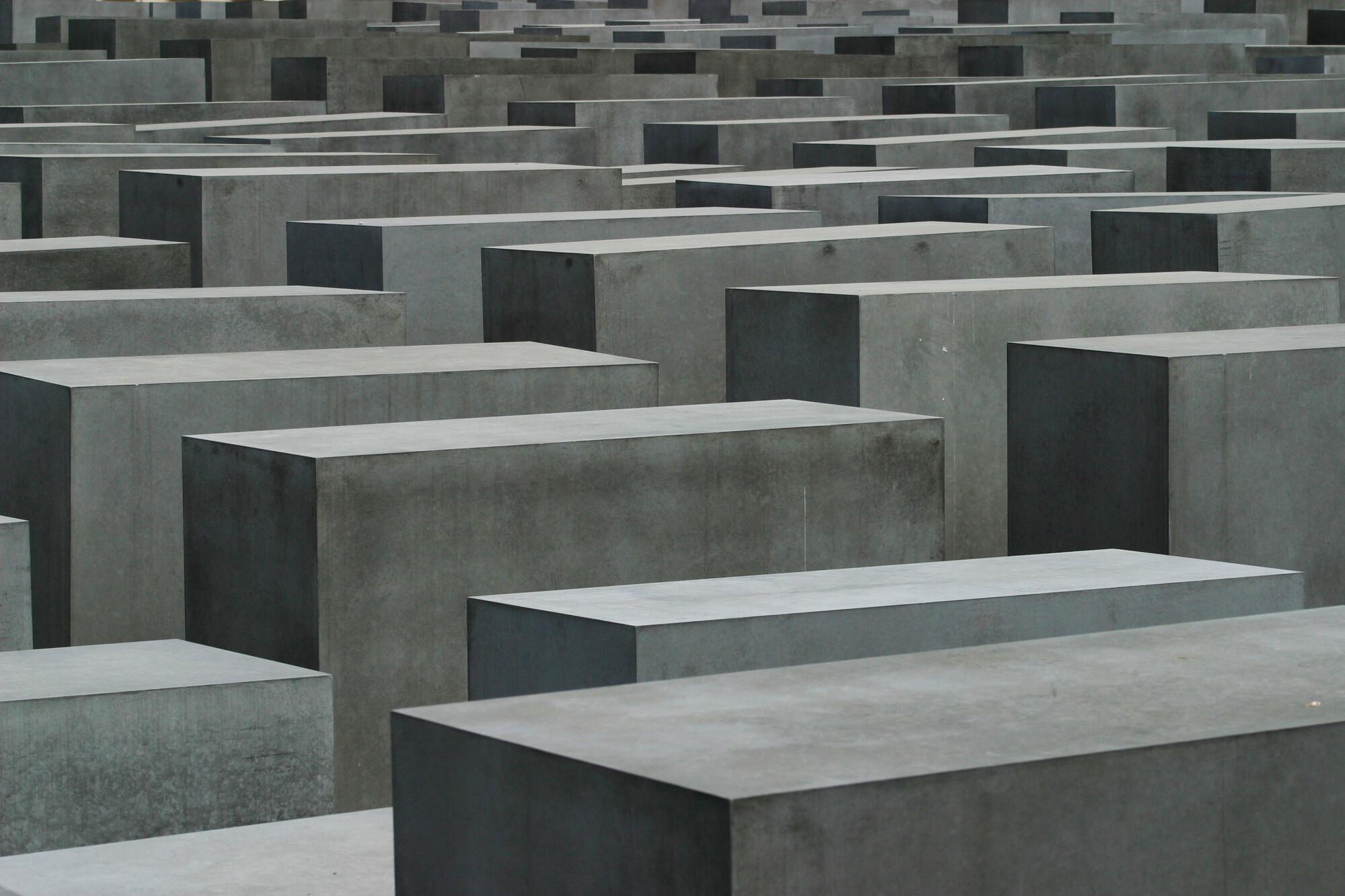 Graue Betonstelen in unterschiedlichen Höhen stehen dicht an dicht in einem rasterförmigen Feld – das Stelenfeld des Holocaust-Mahnmals in Berlin, mit engen Wegen dazwischen und einer nüchternen, beklemmenden Atmosphäre.