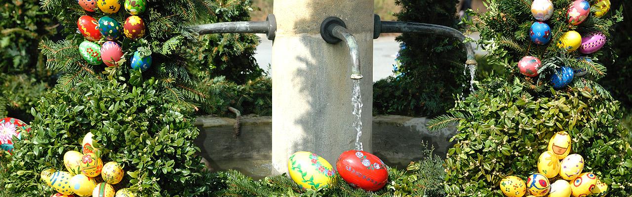 Osterbrunnen Brunnen mit fließendem Wasser aus Hahn, darum Grün und bunte Ostereier