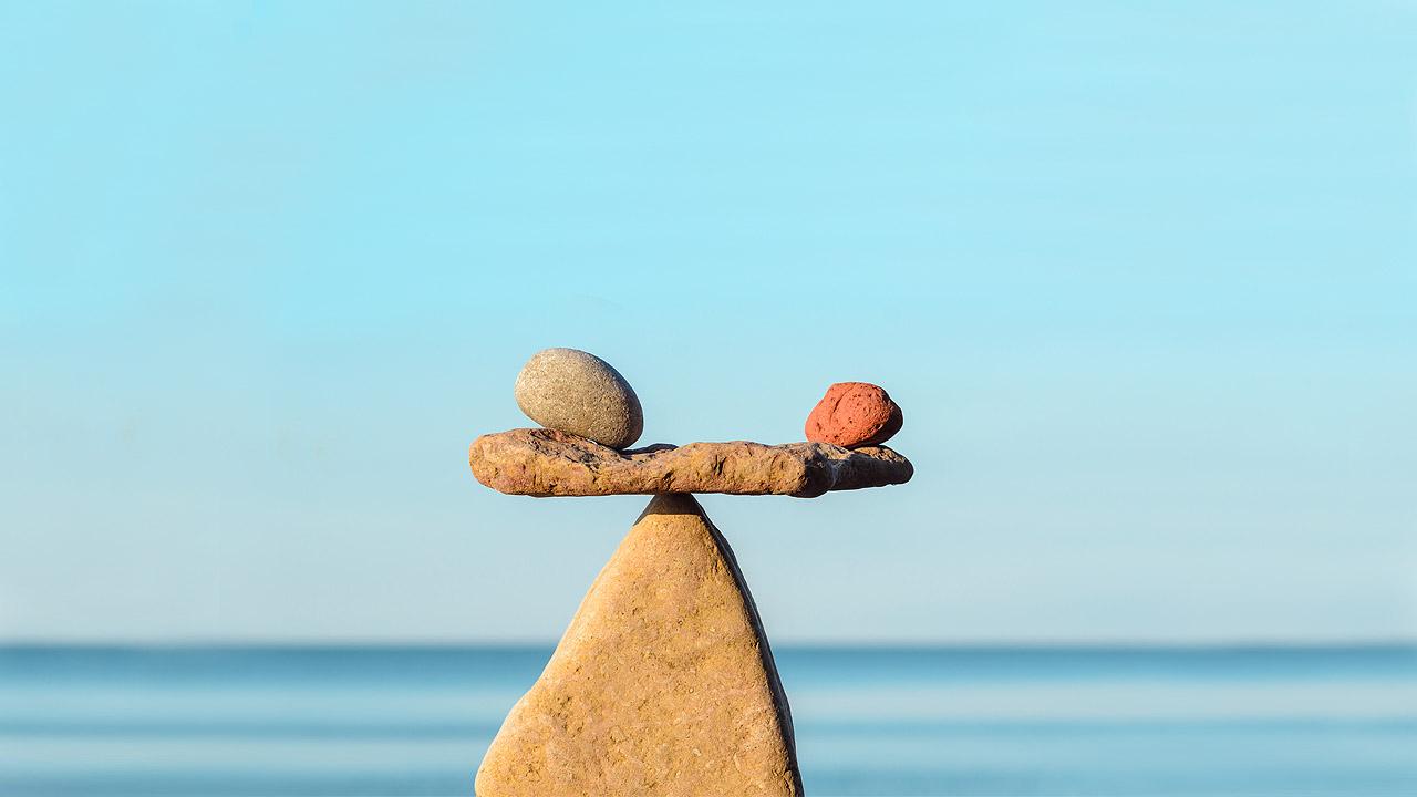 Steinmännchen am Meer in Form einer Waage, auf dem Querstein liegen links und rechts zwei kleiner Steine