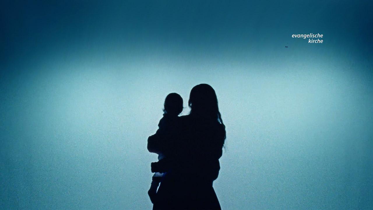 Silhouette einer Mutter mit Kind vor türkisfarbenem Lichtschein