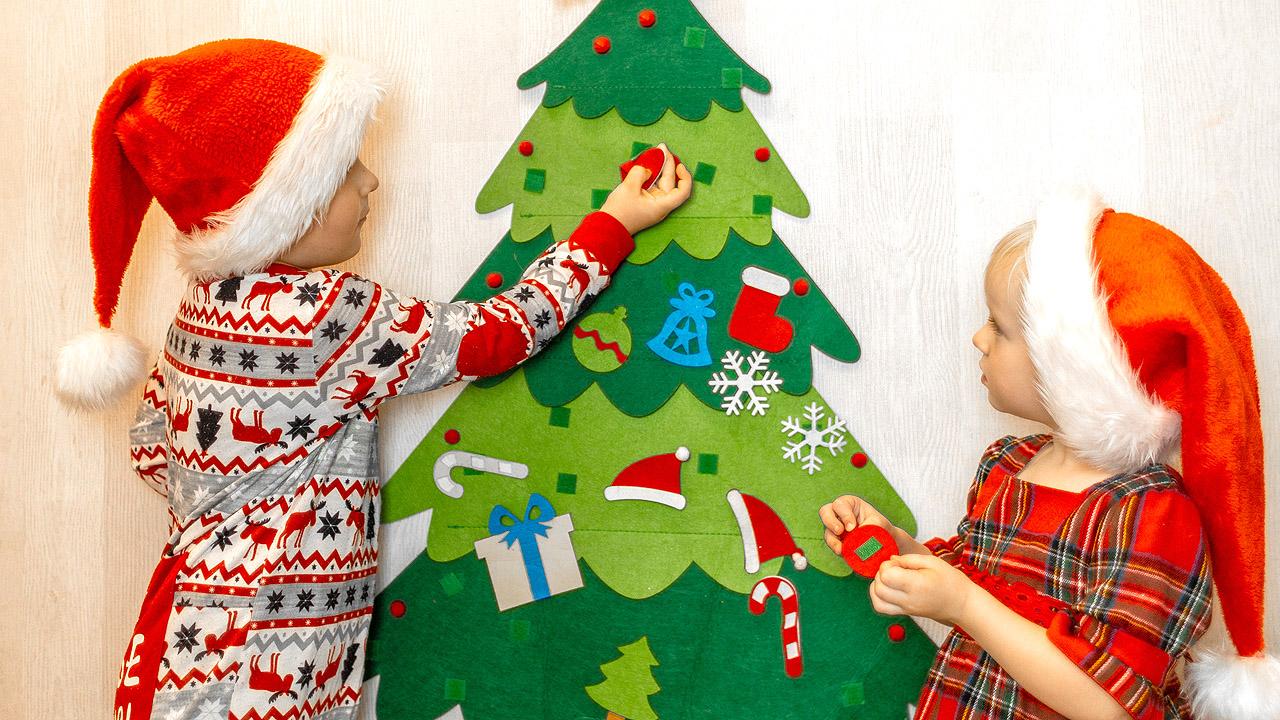 Weihnachtsbaum aus Filz Zwei Kinder schmücken einen Weihnachtsbaum aus Filz mit gefilztem Schmuck