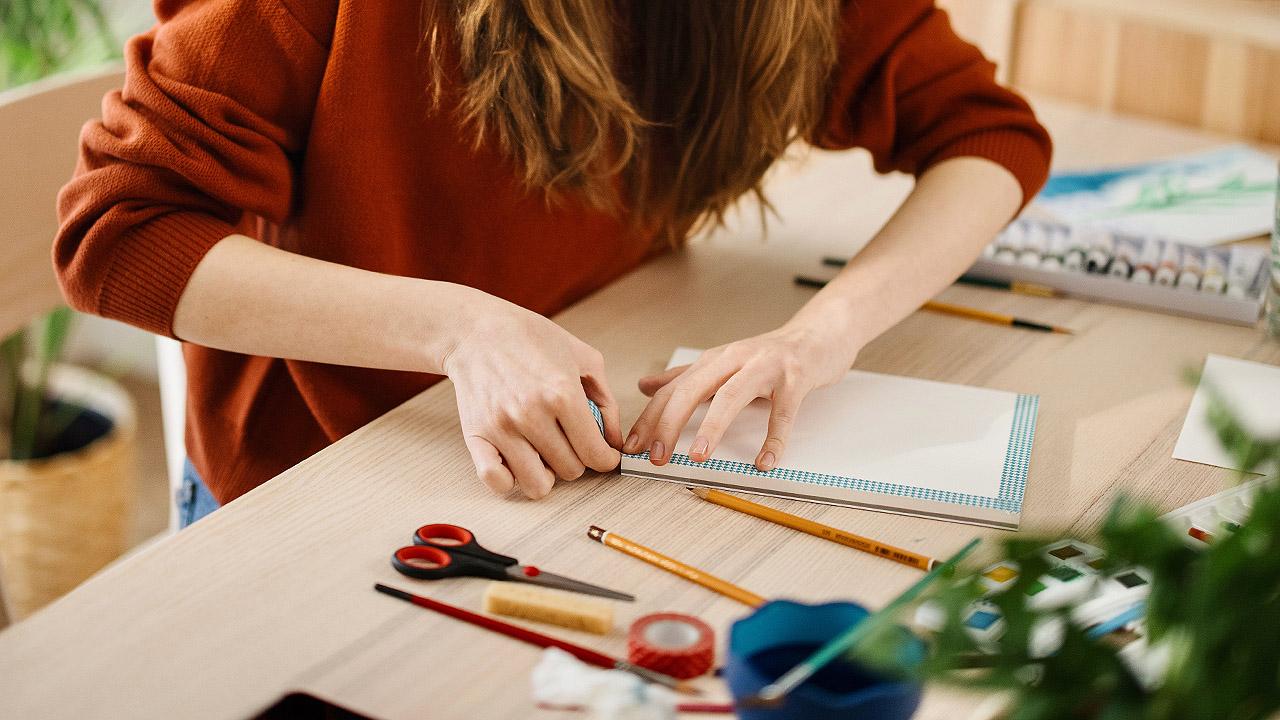 Hände einer Frau berühren Aquarellpapier, daneben liegen Stifte