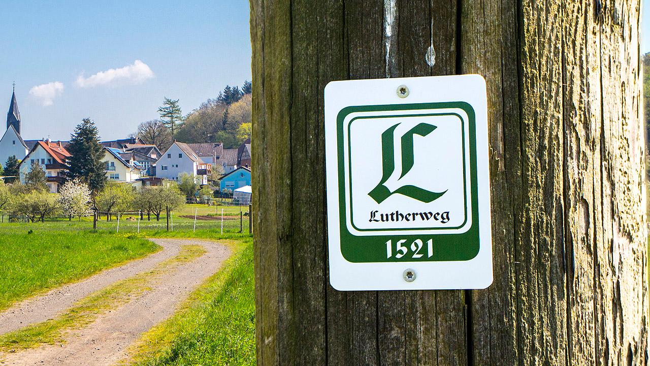 Logo des Lutherweges, dahinter ein Dorf