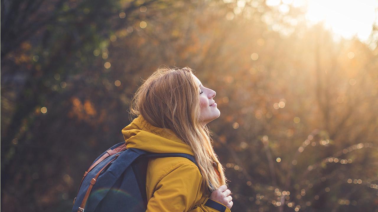 Eine Frau blickt in einer herbstlichen Umgebung Richtung Sonne
