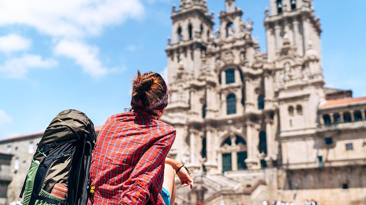Eine Frau mit Rucksack sitzt vor der Kathedrale in Santiago