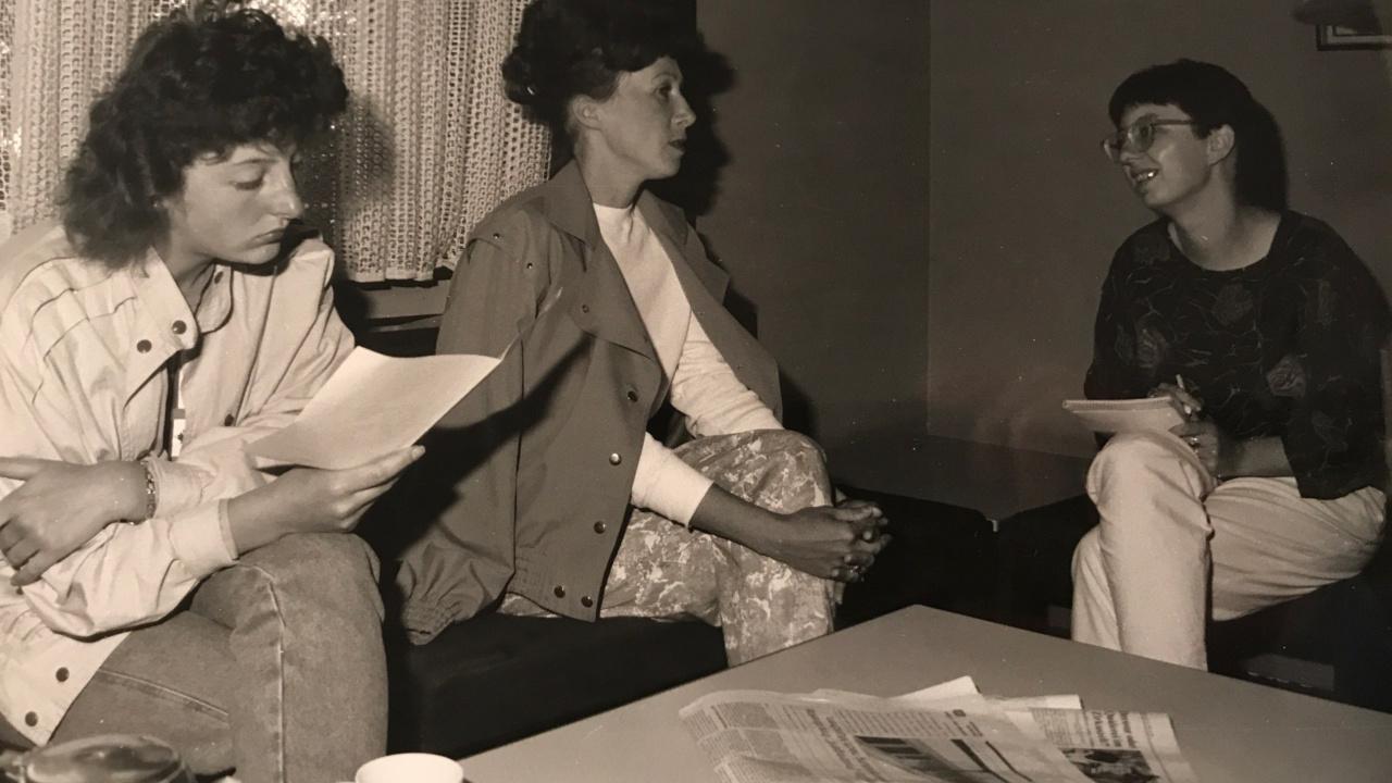 Antje Schrupp 1990 Antje Schrupp sitzt mit einem Schreiblock auf dem Schoß rechts und spricht mit zwei Frauen, die links von ihr sitzen. Eine hält ein Blatt Papier in der Hand und schaut daraufd
