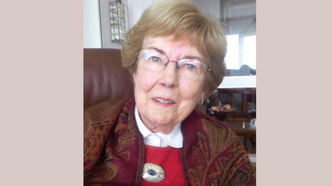 Christa Springe 2018 Christa Springe trägt einen roten Pullover mti goldener Brosche und einer gemusterten Jacke. Sie hat kurze graubraune Haare und eine goldene Brille