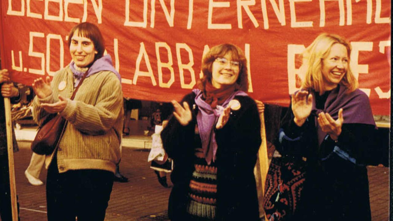 Frauen für den Frieden Demo 1984 Drei Frauen demonstrieren vor einem roten Plakat mit gelber Schrift für den Frieden und klatschen dabei in die Hände
