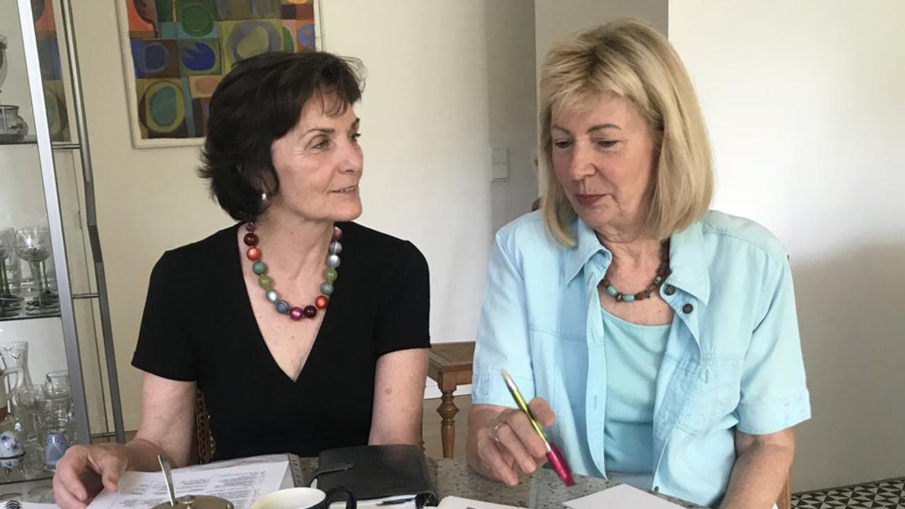 Helga Engler-Heidle und Ute Knie An einem Tisch in einer Küche sitzen Helga Engler-Heidle und Ute Knie sie haben Papiere vor sich auf dem Tisch liegen.