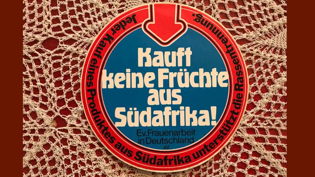 Kauft keine Früchte aus Südafrika Aufkleber rund mit blauem Grund und rotem Rand auf einer Häkeldecke gelegen