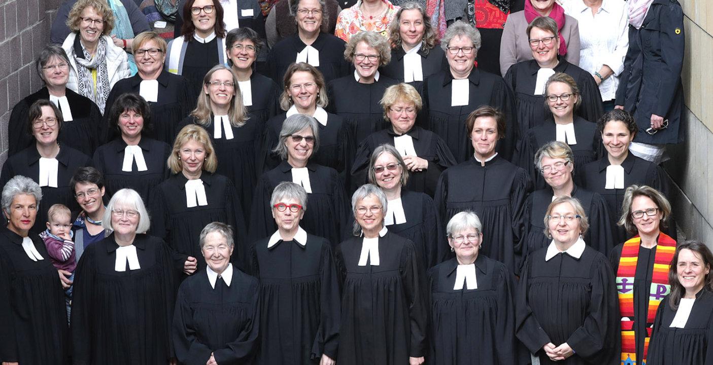 Pfarrerinnen der EKHN Eine große Zahl von Pfarrerinnen im schwarzen Talar stehen auf einer Treppe und blicken ins Bild.