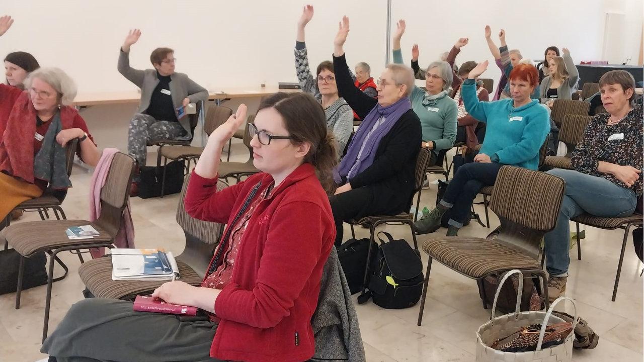 Pfarrerinnentag Resolution 2023 Frauen sitzen in einem Saal und heben die Hand zur Abstimmung.