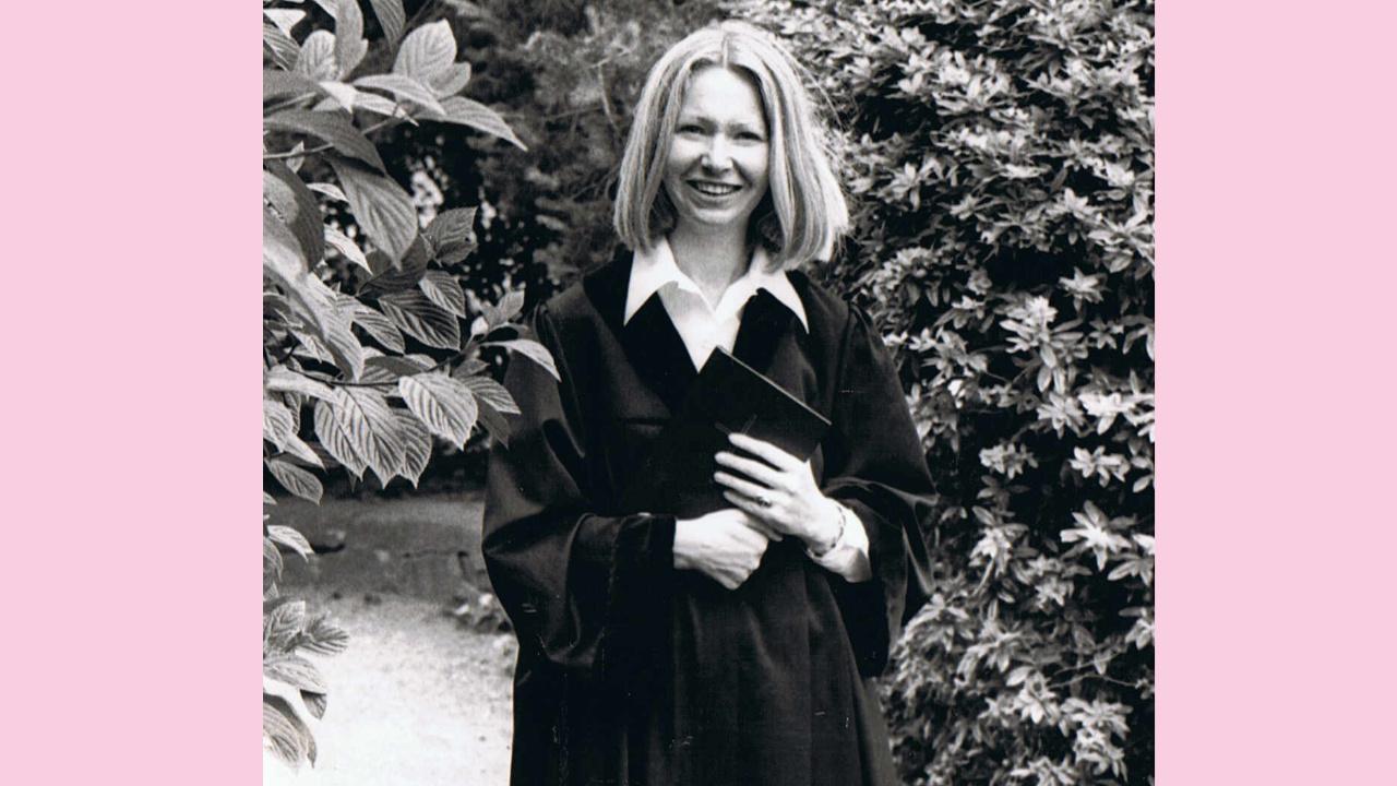 Pfarrvikarin Ute Knie Ute Knie trägt einen schwarzen Talar mit weißem Kragen und steht vor einem Busch