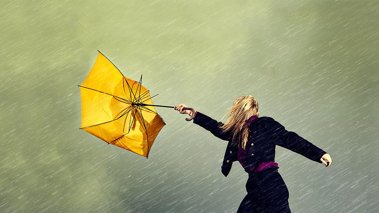 Der Wind bläst gegen einen gelben Regenschirm, den eine Frau noch gerade in der Hand hält und stülpt ihn um