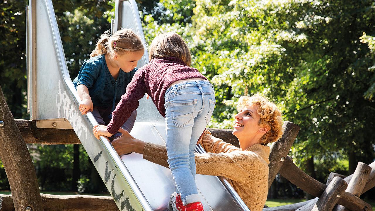 Mutter-Kind-Kur Eine Mutter spielt an einer Spielplatz-Rutsche mit ihren beiden Töchtern
