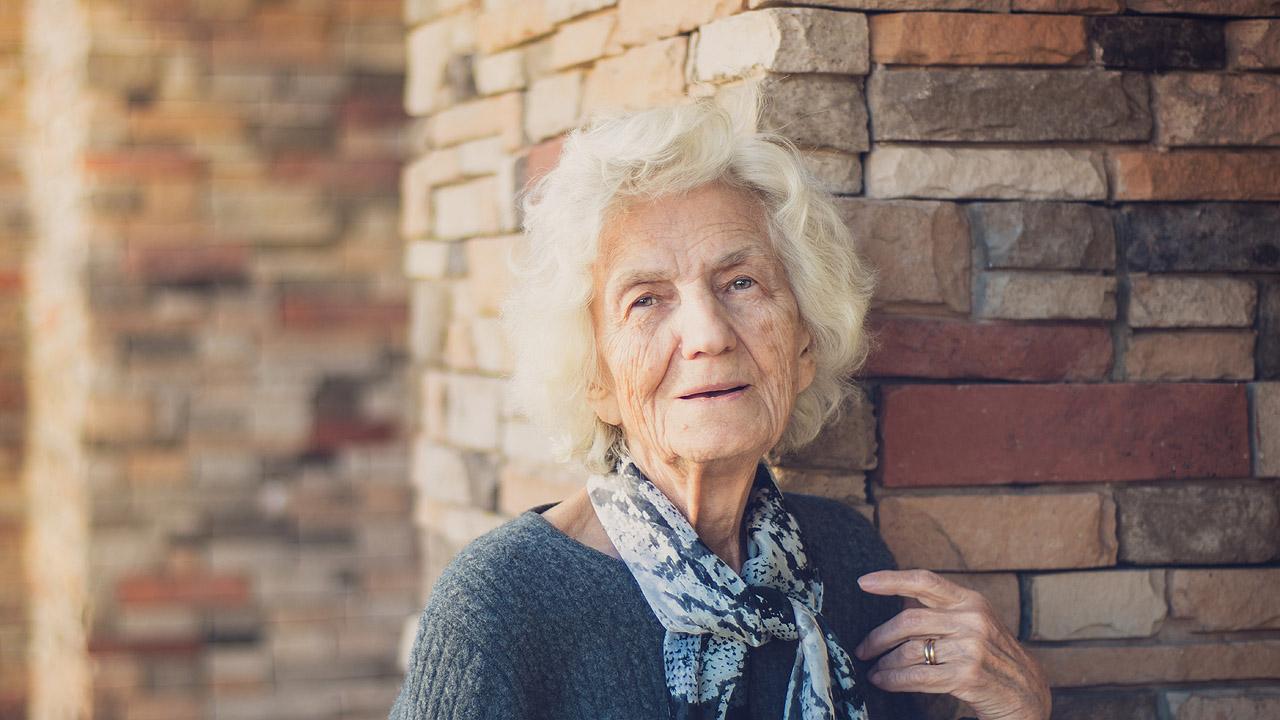 Seniorin Eine ältere, weißhaarige Dame vor einer Mauer