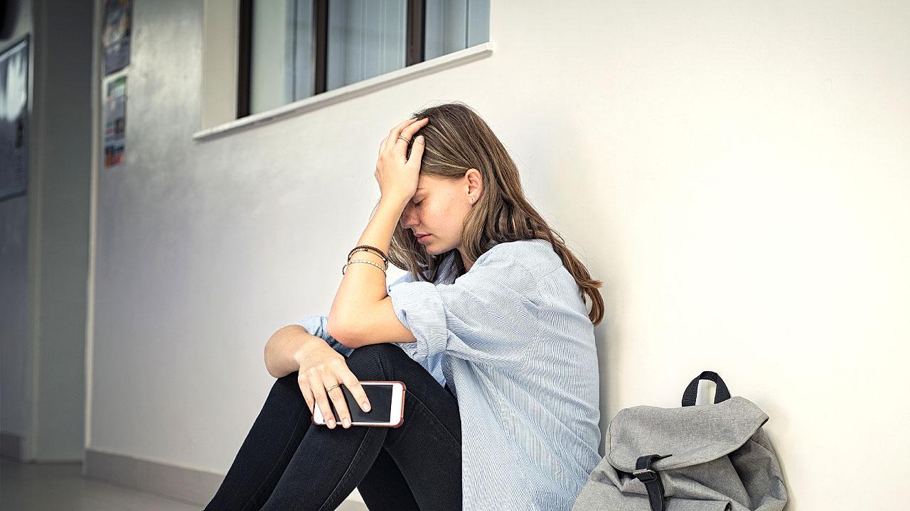 Ein Mädchen sitzt am Boden und verbirgt den Kopf in den Händen