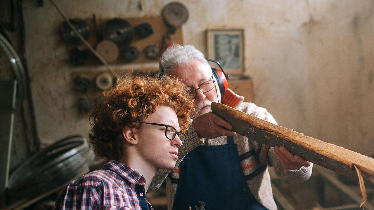 Holzwerkstatt Ein Meister zeigt einem Lehrling etwas auf einem Holzbrett