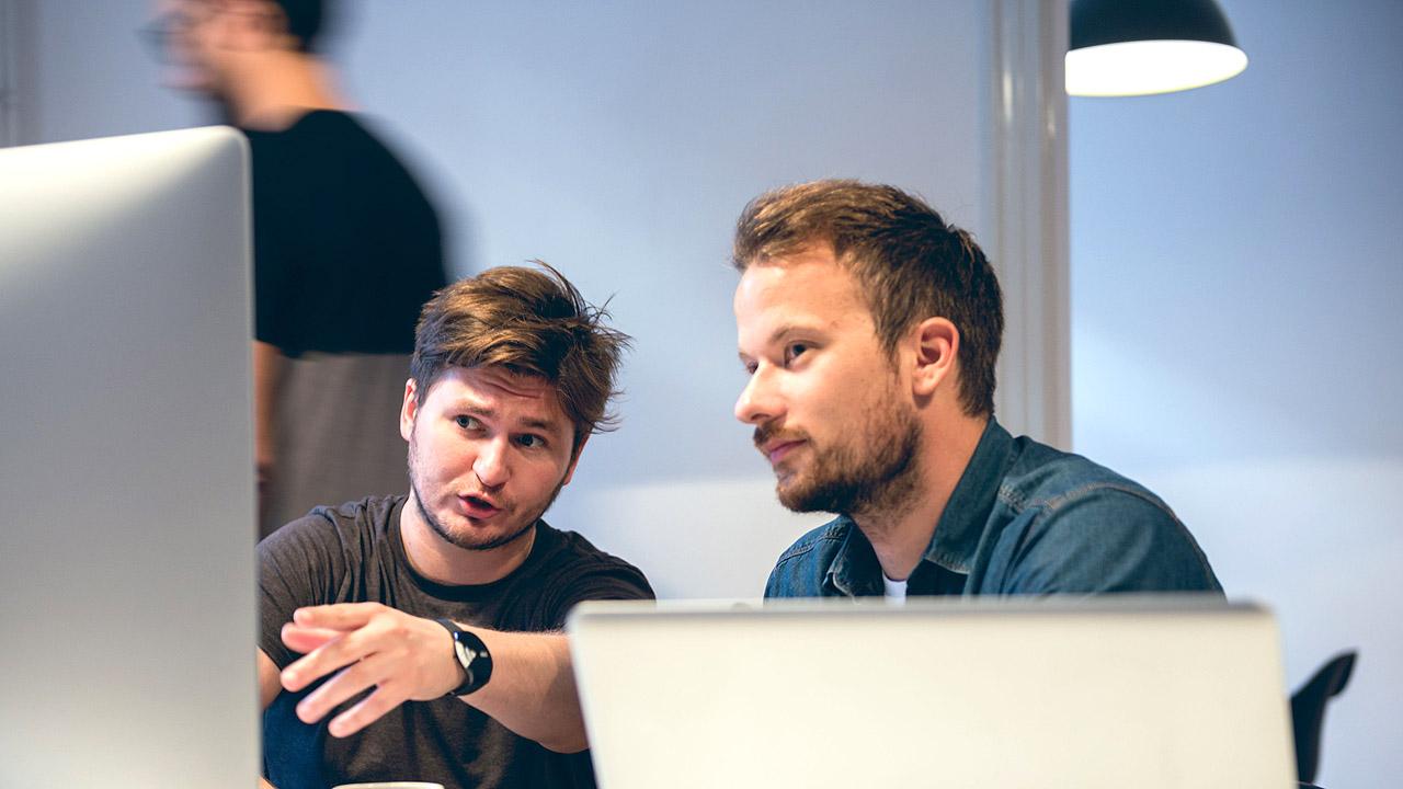 2 Männer am PC, die miteinander sprechen