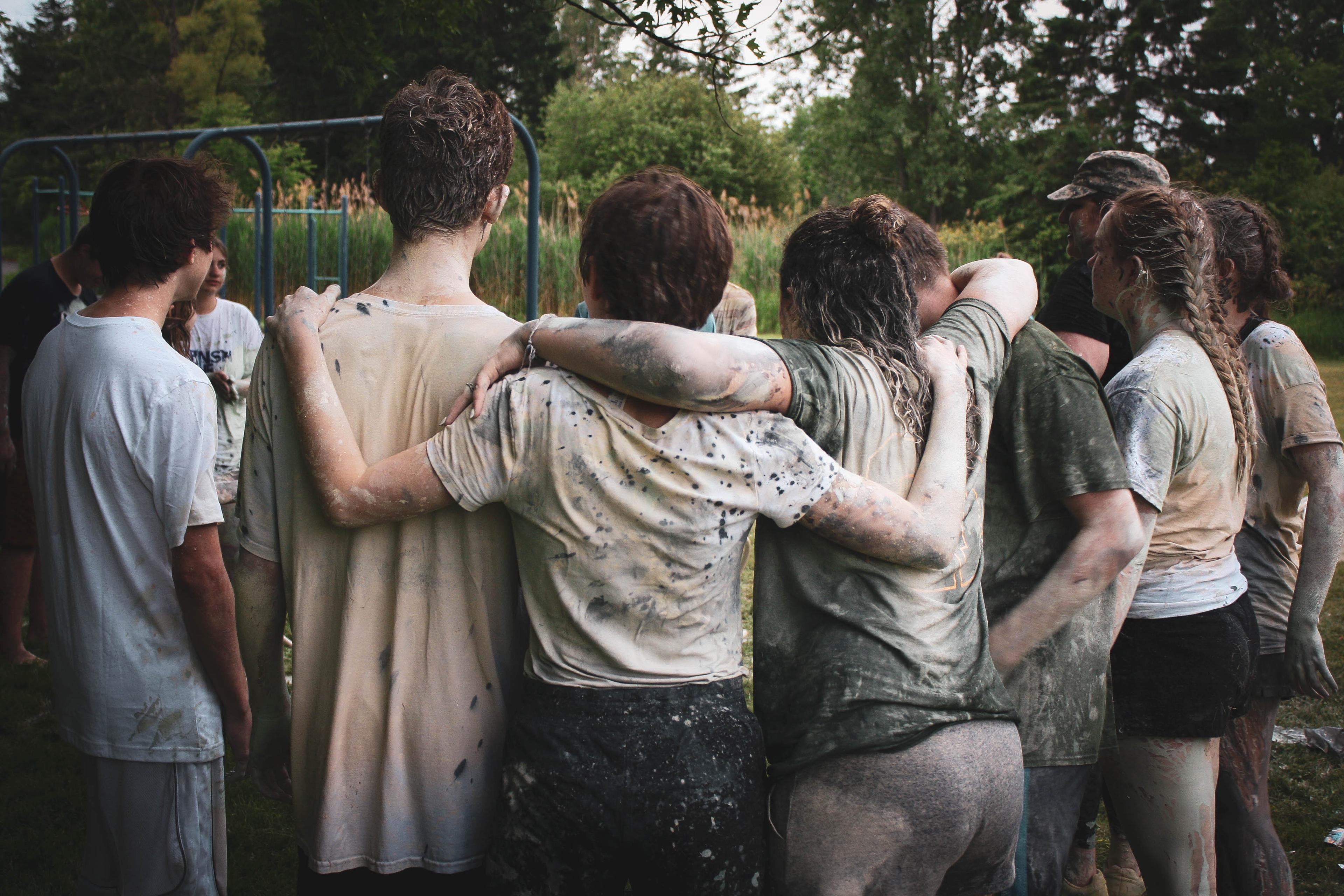 Gruppe junger Menschen, die sich teilweise umarmen. Mit verschmutzter Kleidung.