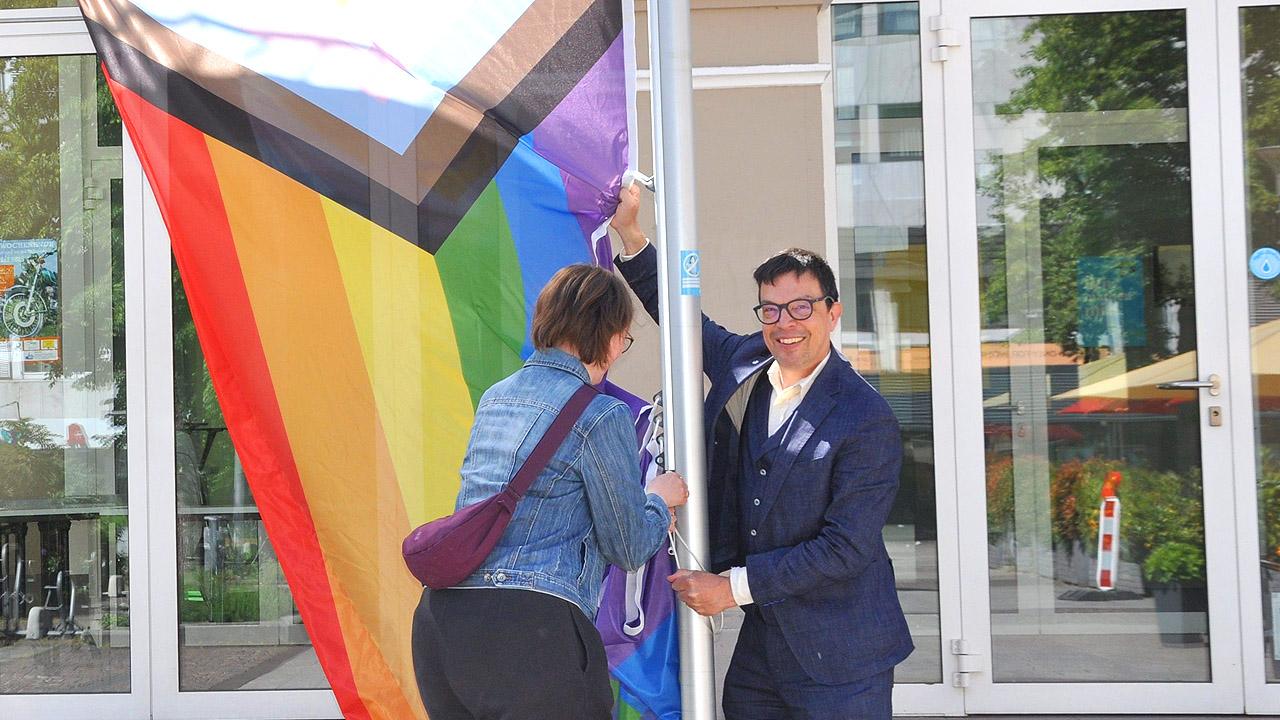 Zwei Menschen ziehe eine bunte Flagge an einem Mast hoch