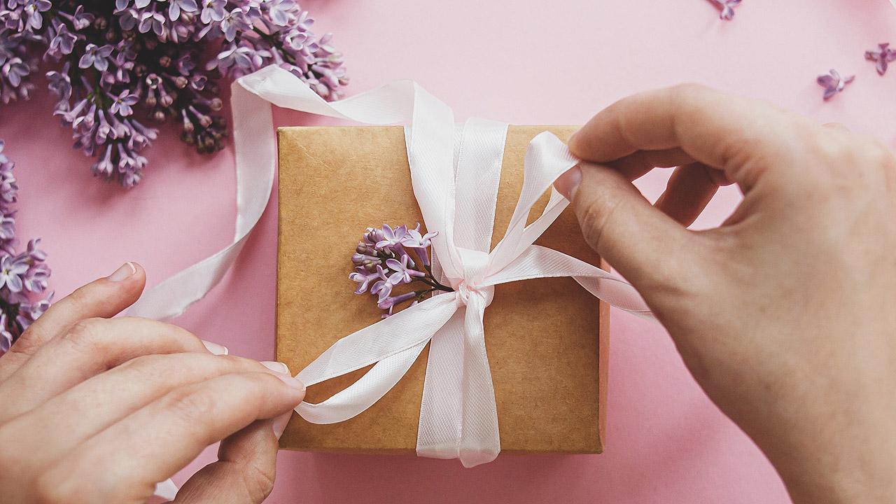 Hände binden eine Schleife um ein Geschenk