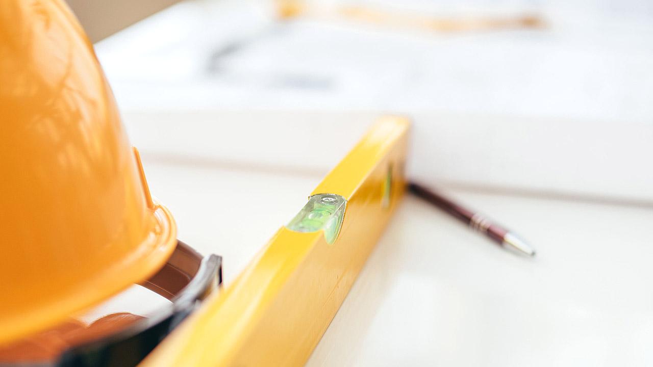 Gelber Schutzhelm und eine Wasserwaage auf einem Tisch