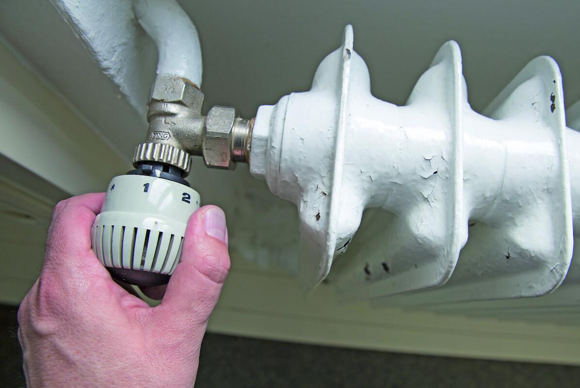 Eine Hand stellt die Temperatur an einer Heizung ein