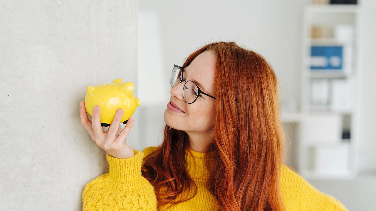 Eine Frau hält ein gelbes Sparschwein in der Hand und lächelt es an