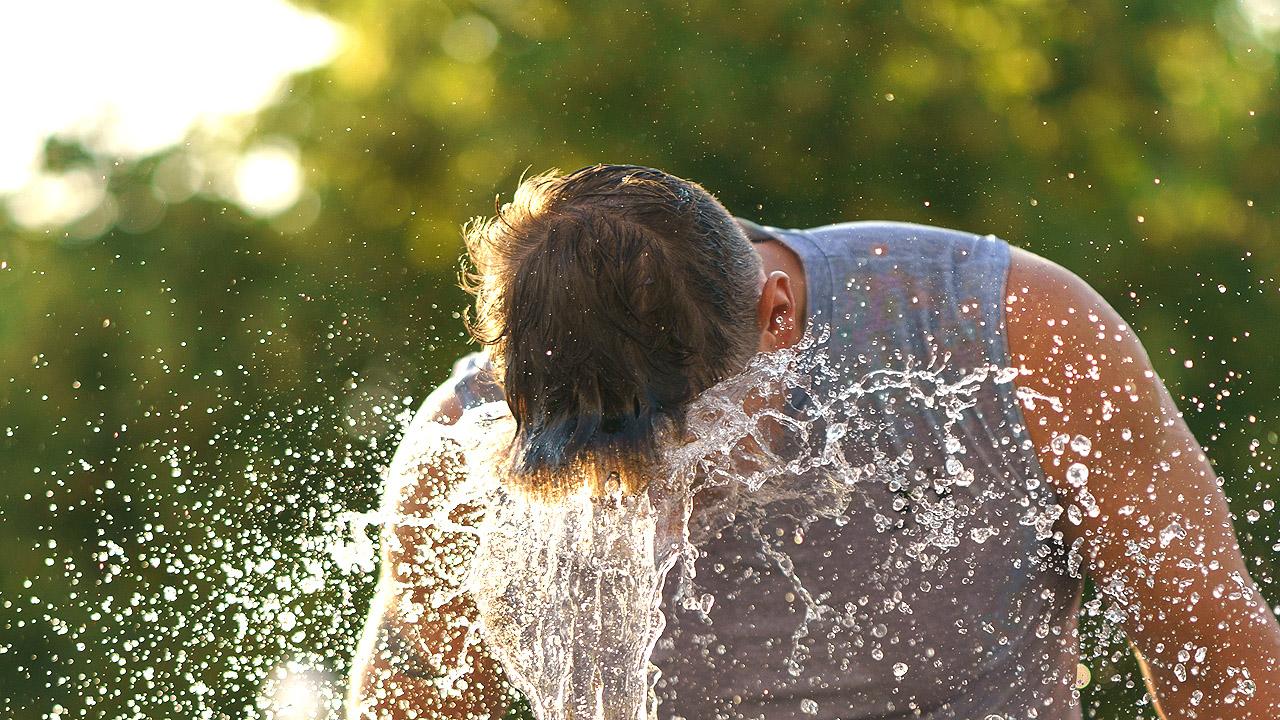 Ein Mann kühlt sich an einem Springbrunnen ab