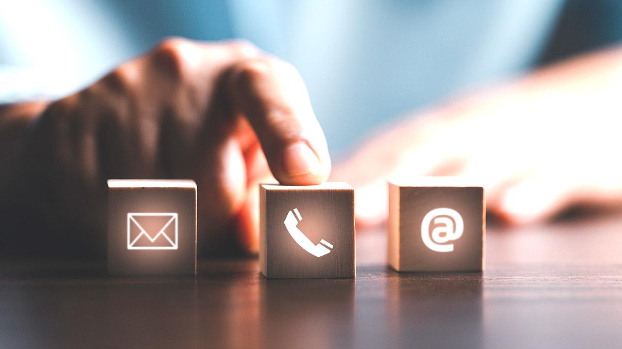Eine Hand zeigt auf ein Brief-, Telefon- und Mailsymbol