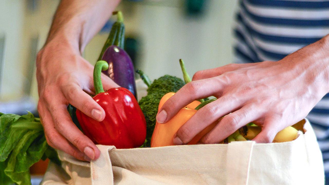 Zwei Hände räumen das Obst und Gemüse aus einer Einkaufstasche aus