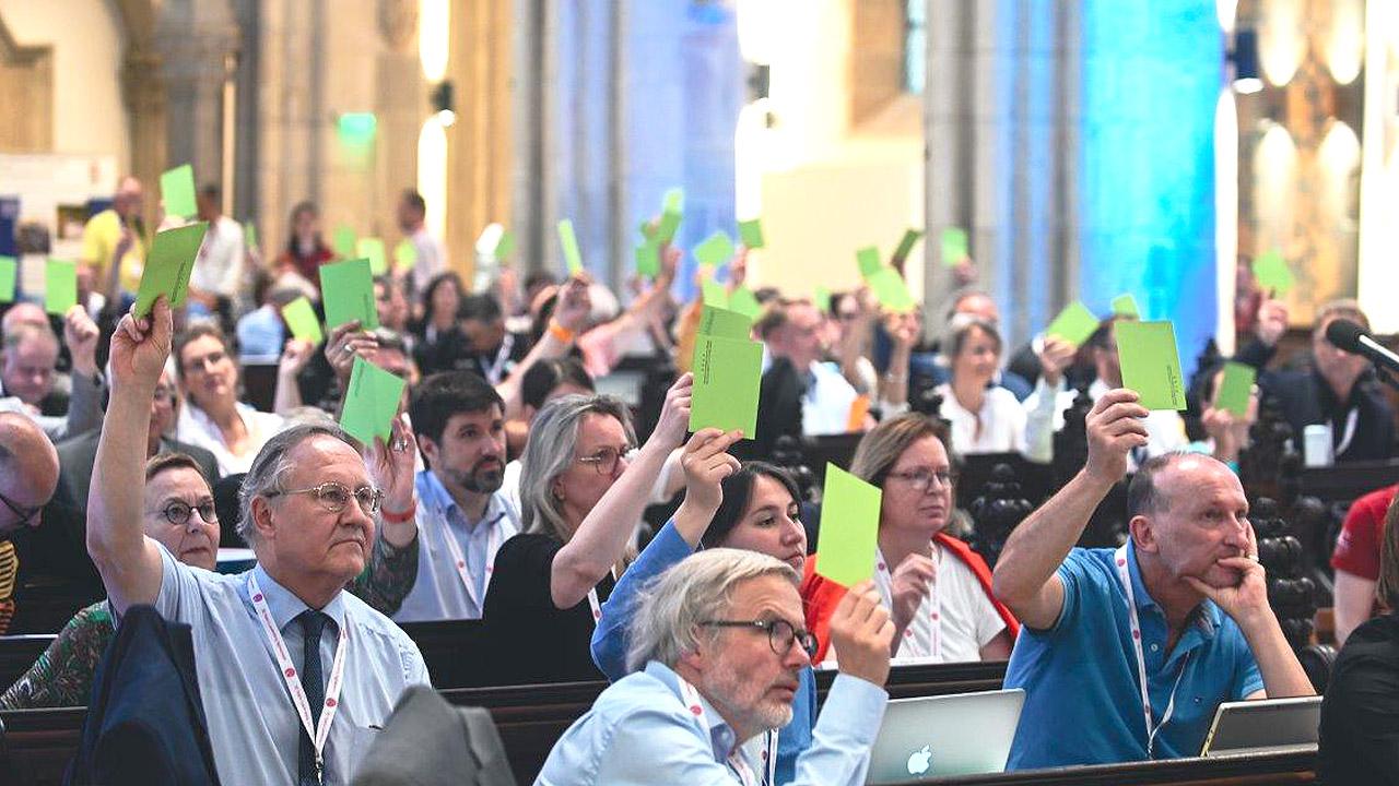GEKE Viele Menschen heben in einer Kirche einen grünen Zettel in die Luft