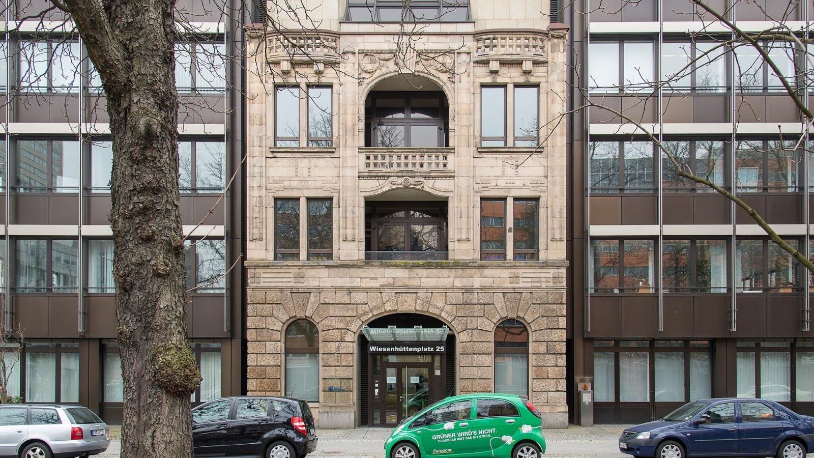 Ansicht der historischen Gebäudefassade inmitten von Neubauten.