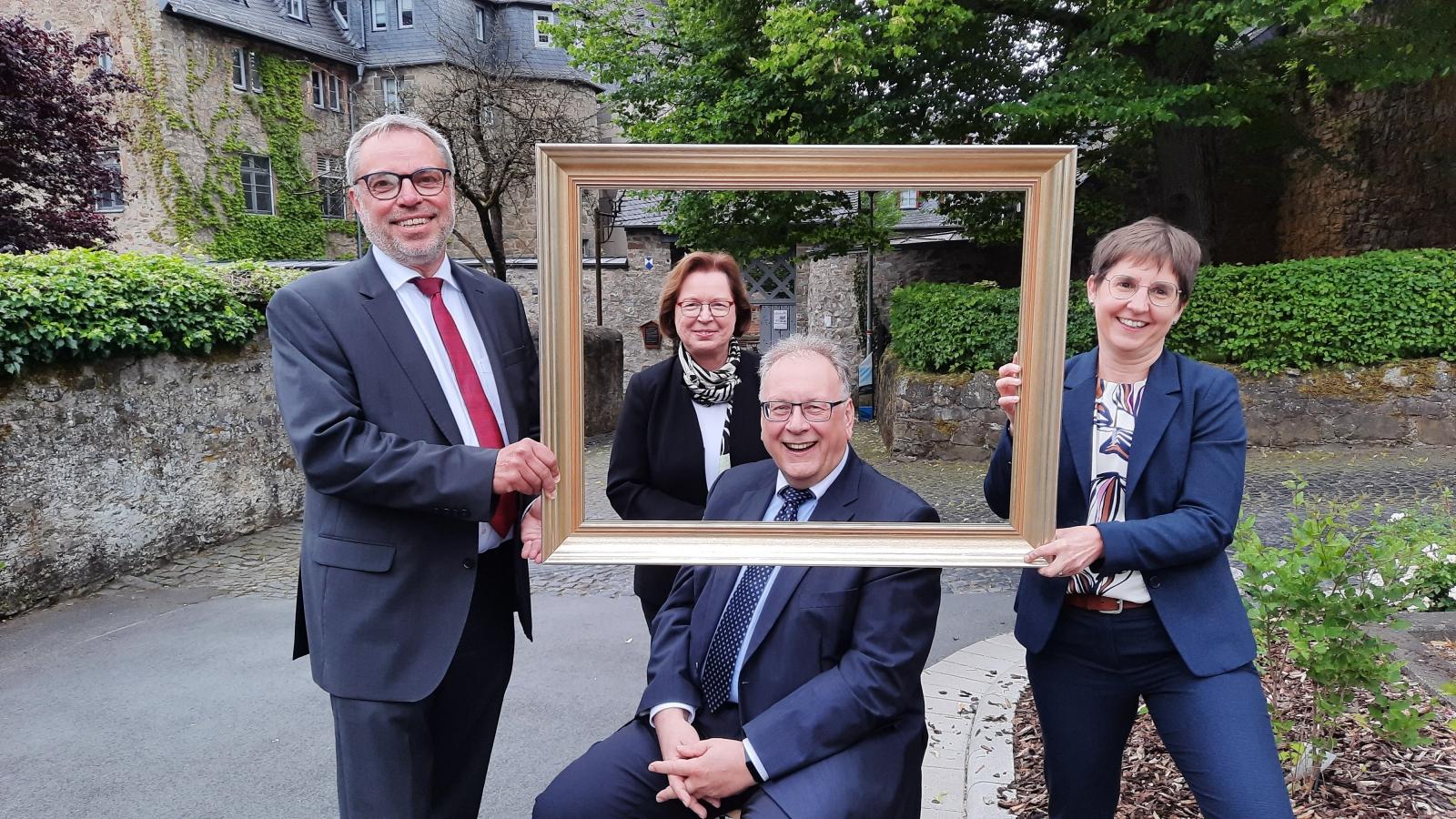 Thorsten Moos Bilderrahmen Kolleginnen halten einen leeren Bilderrahmen, in dem man dann Thorsten Moos sieht.